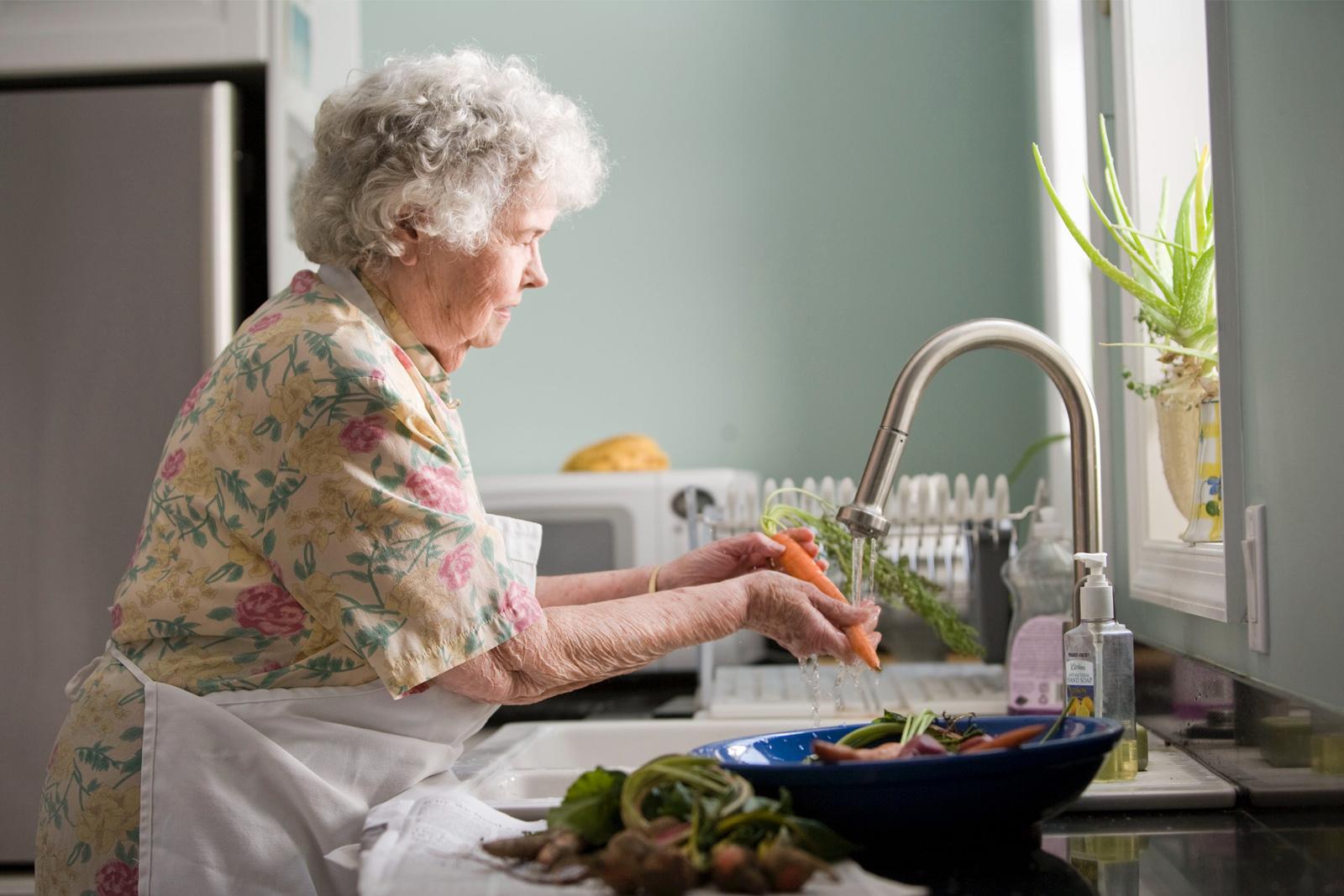 Elderly lady washing vegetables at a sink
